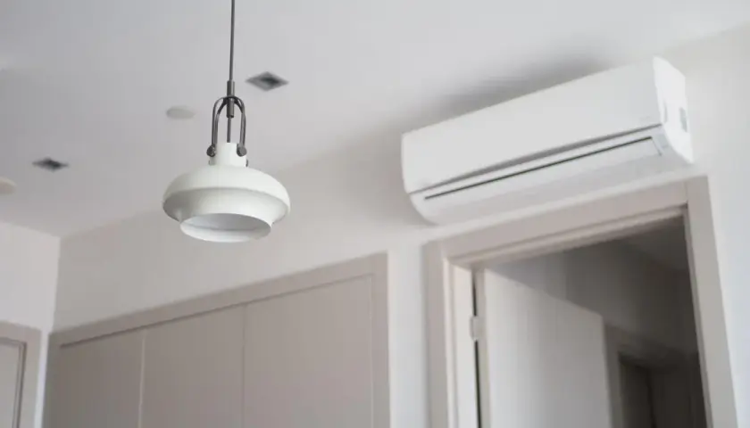Biała jednostka klimatyzacyjna zamontowana na ścianie nad drzwiami, obok lampy wiszącej.